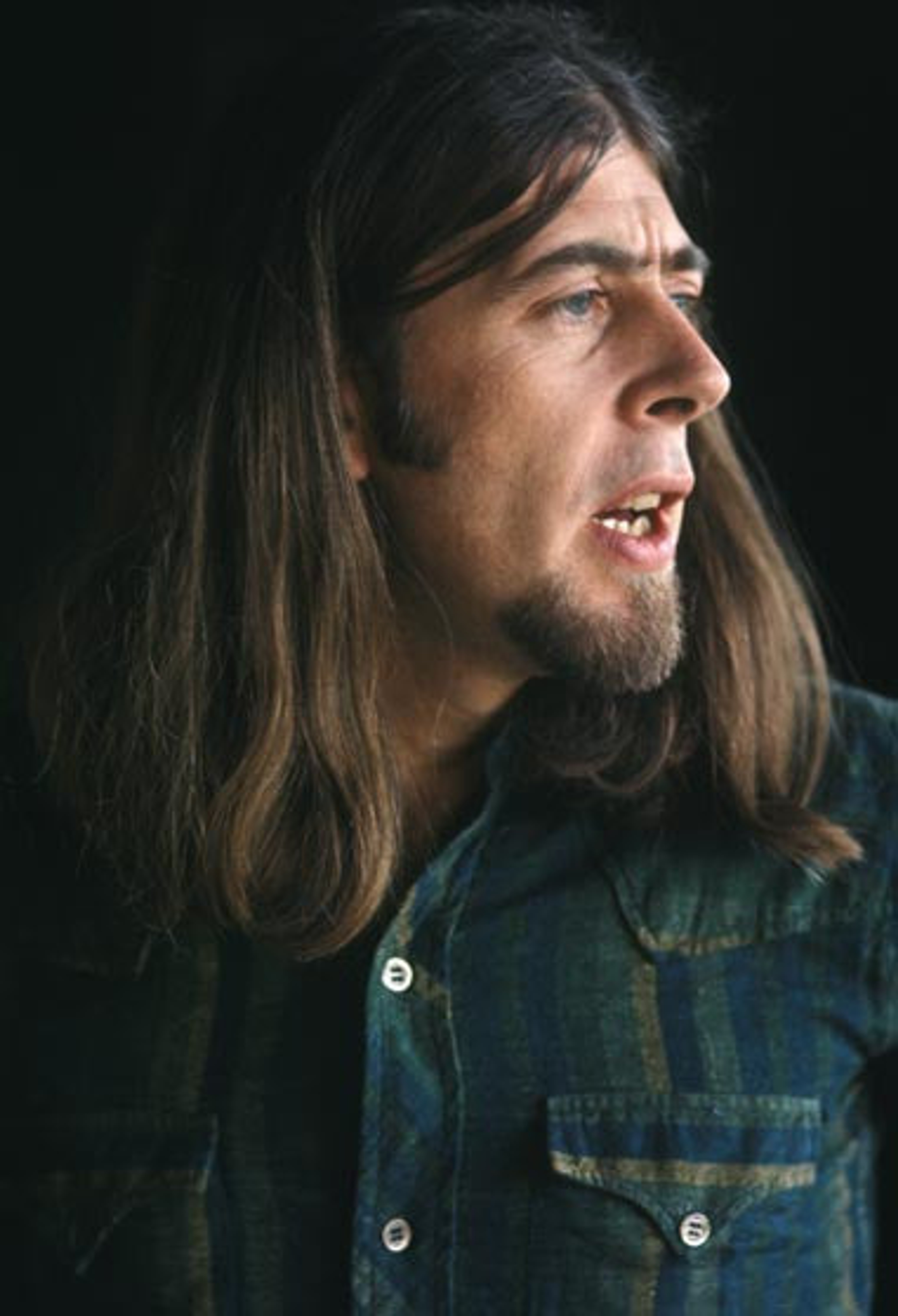 Photo of John Mayall. He has long brown hair and is turning to the left to look over his shoulder