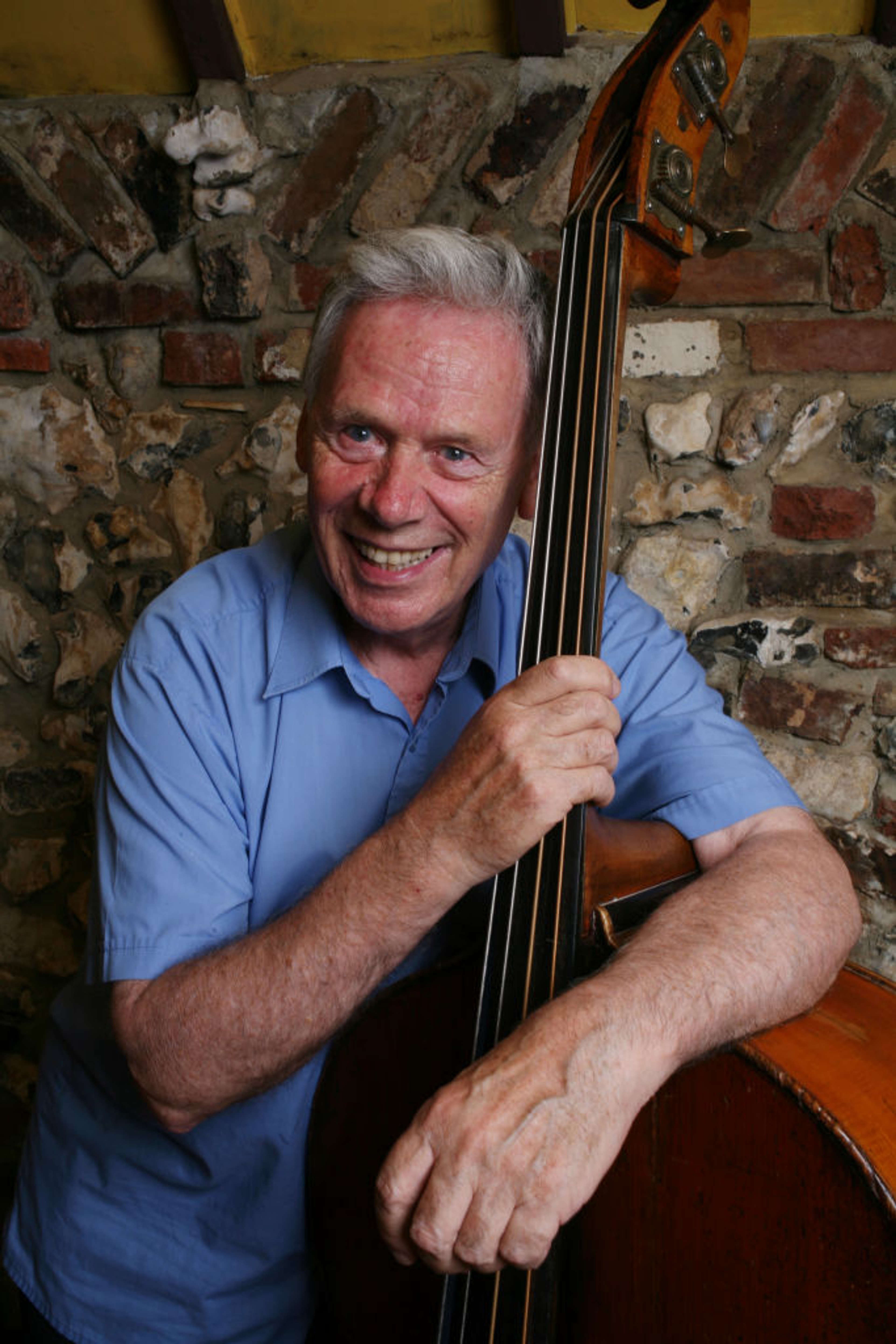 Photo of Herbie Flowers. He is wearing a blue shirt and holding a stand up bass. Photo from Getty Images