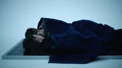 Metahaven, Chaos Theory film still from 2021 showing two people on the floor sleeping under a dark navy blanket