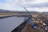 Drone view of workers on roof securing sections while crane moves metal roofing into place