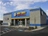 Outside corner view of Napa Auto Parts store on a sunny day. The building is metal and concrete with grey, clue, and yellow coloring and the Napa Logo.