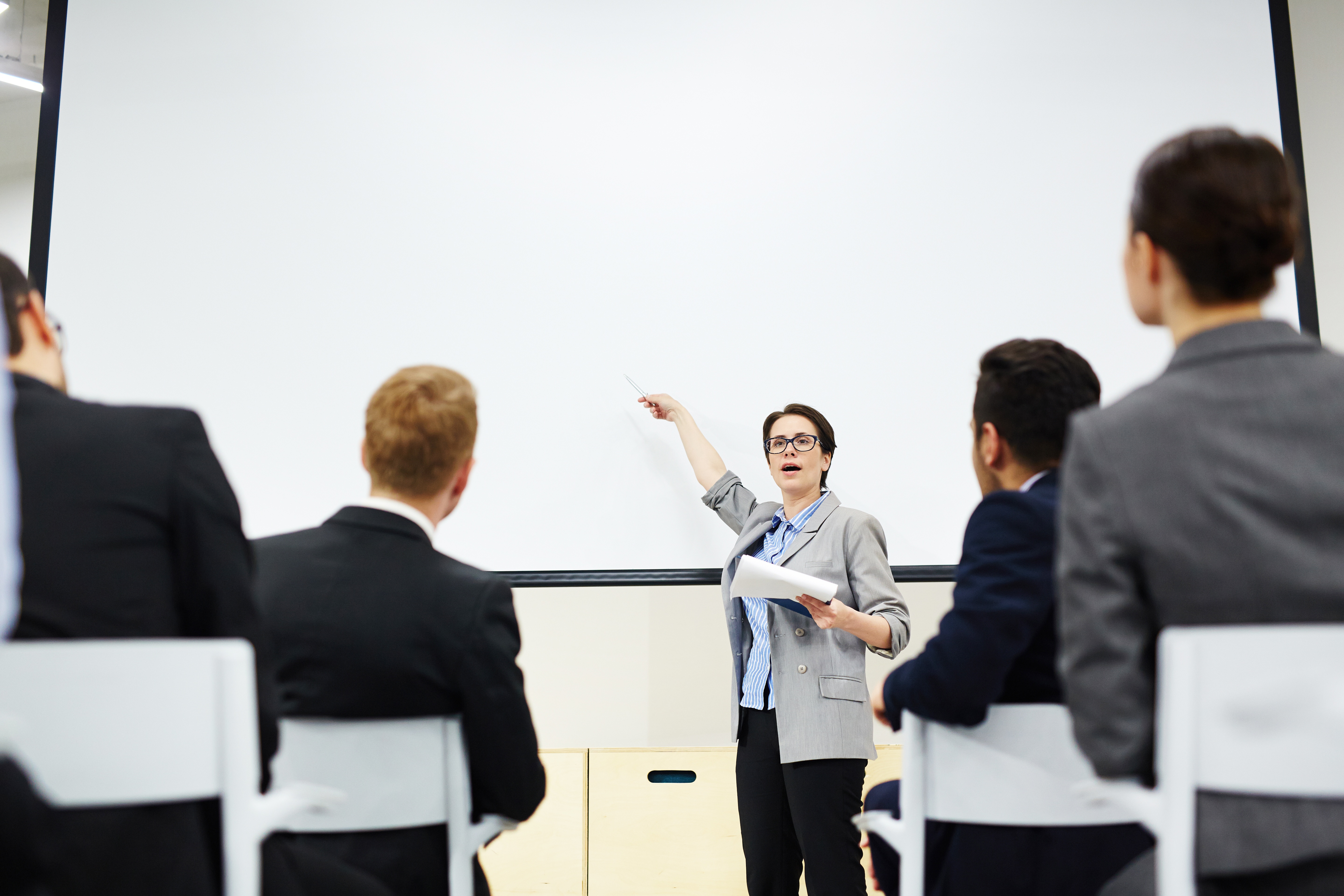 Seorang wanita sedang memamerkan skill public speaking dengan cara presentasi di kantor.