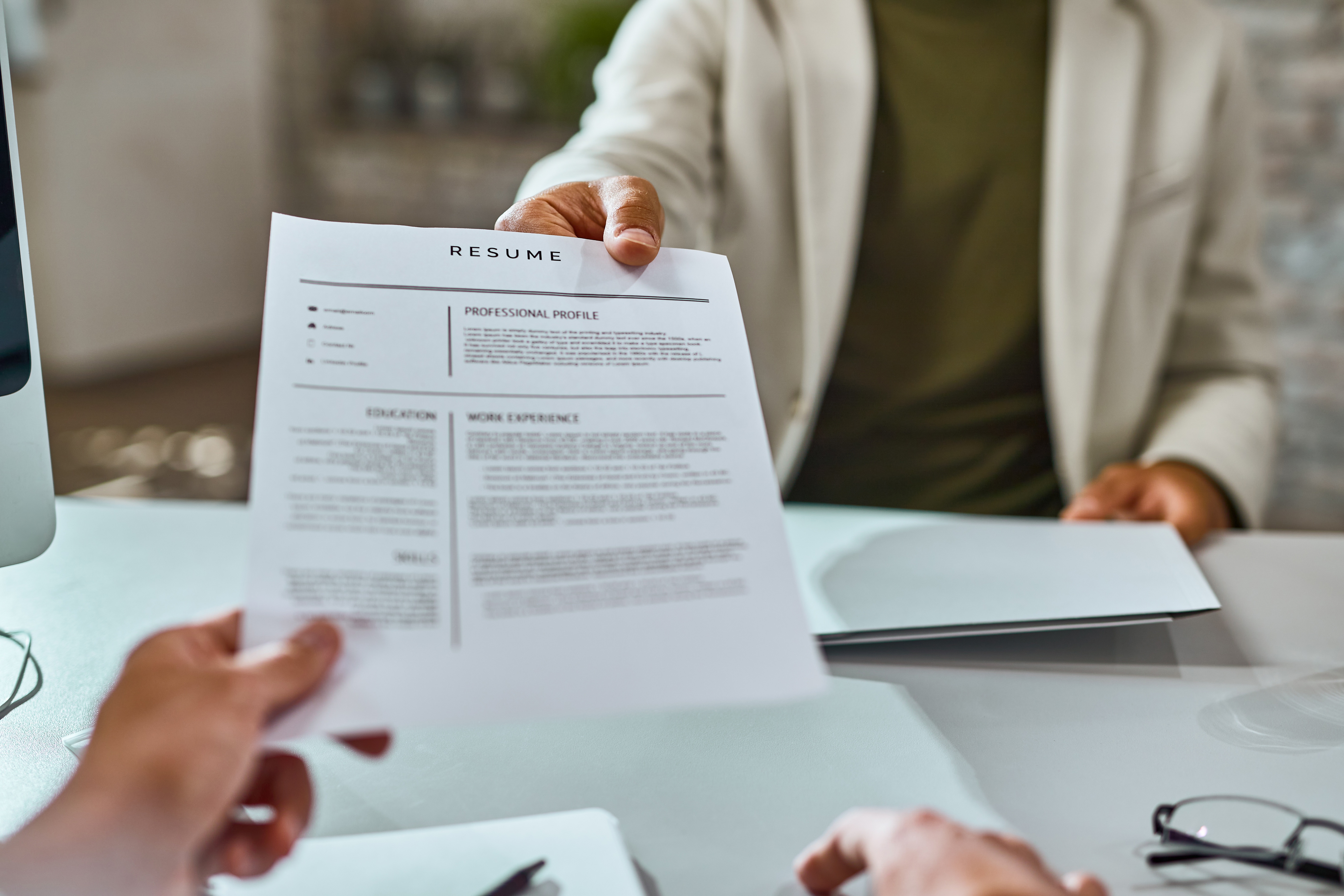 A job applicant hands over their resume during an interview, with selection criteria showcasing their qualifications and alignment with job requirements.