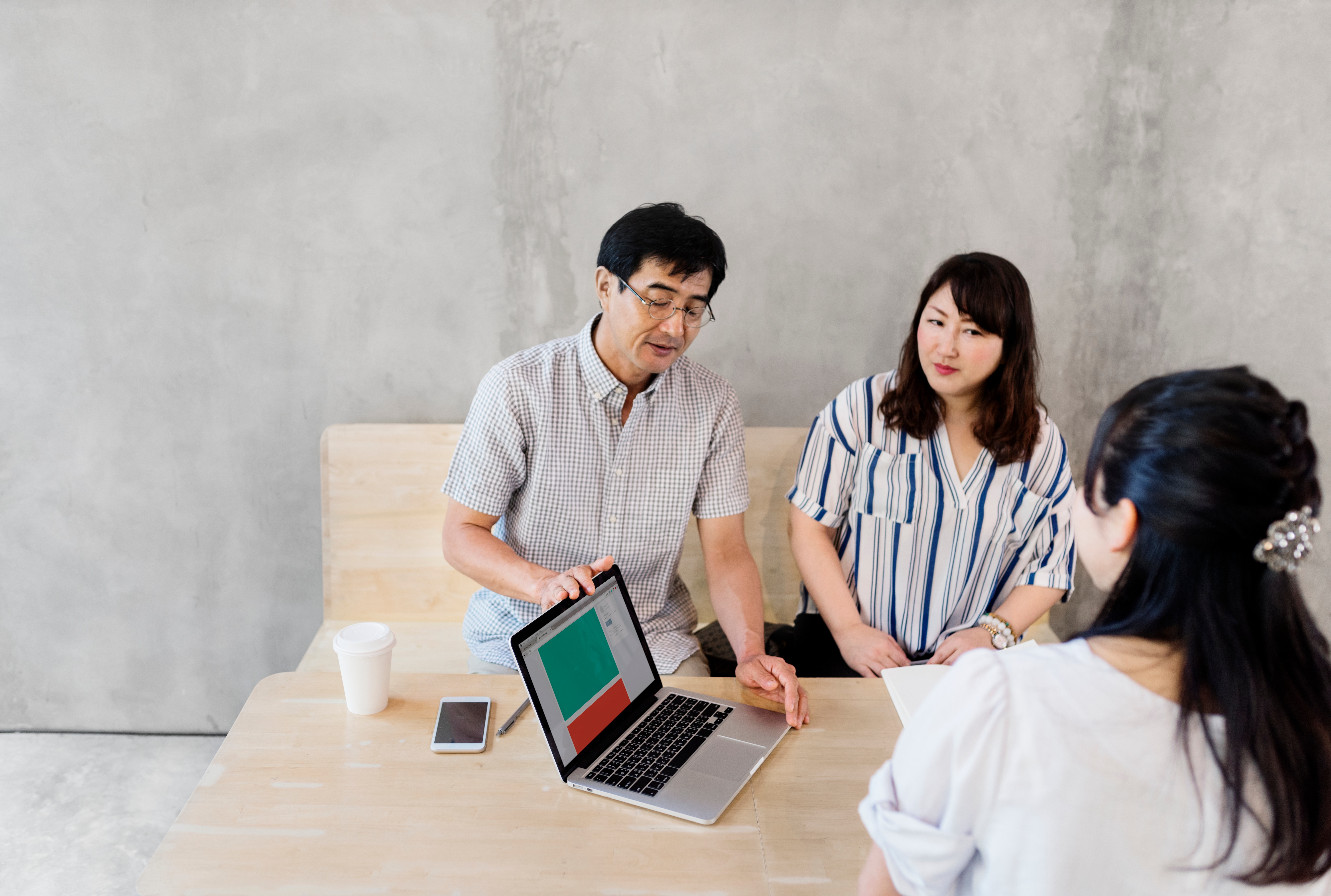 Satu orang mempresentasikan data di laptop secara duduk dan dua orang lainnya memerhatikan sambil duduk