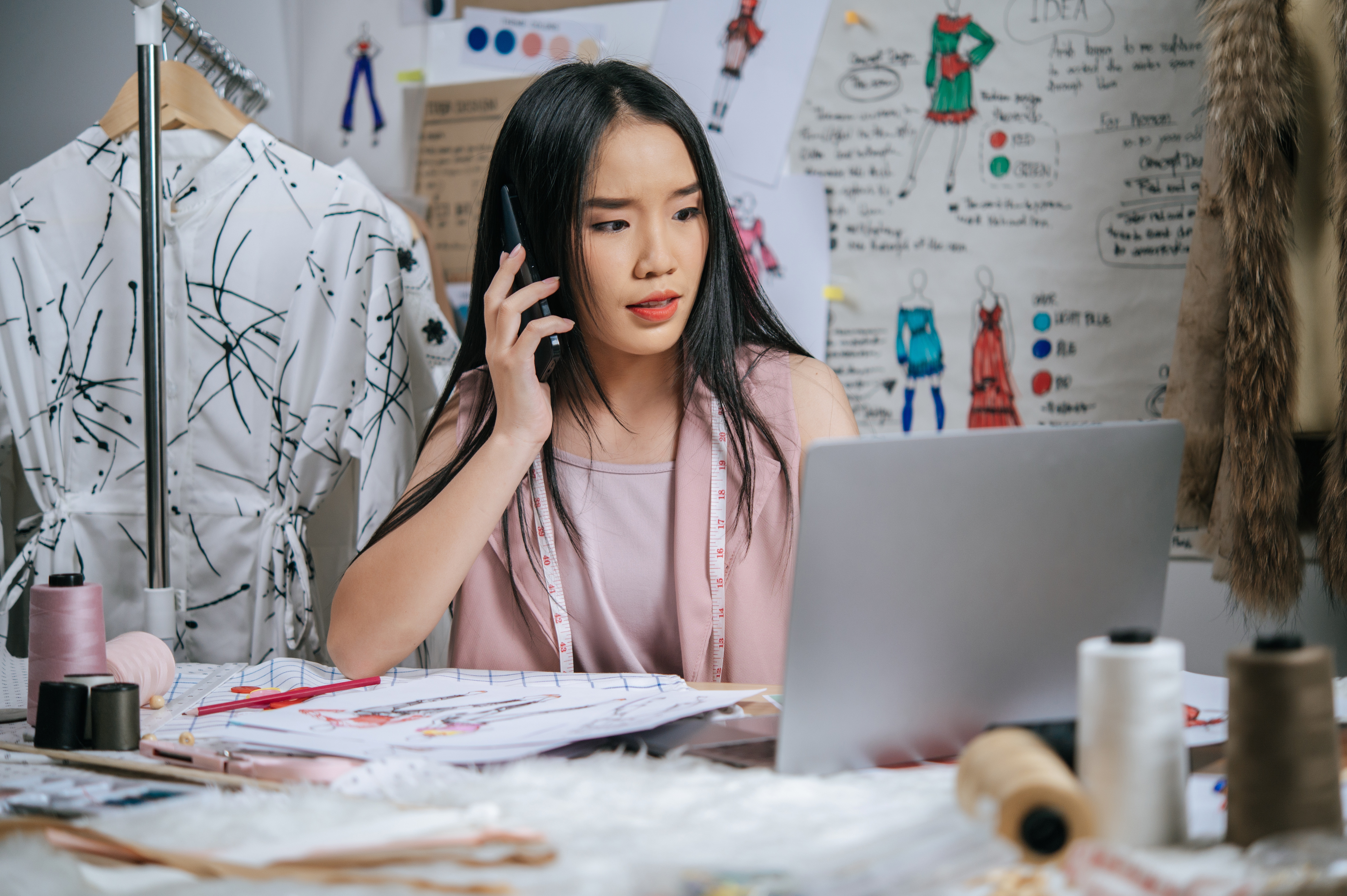 Wanita berbincang di telefon bimbit sambil melihat komputer riba di depannya.