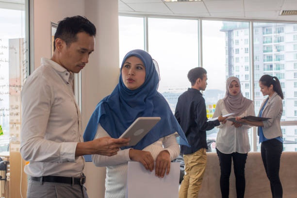 Dua individu serius berbincang dengan menggunakan tablet di pejabat. 