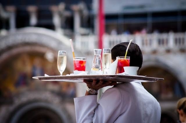 Seorang waiter sedang mengantar minuman pesanan pelanggan ke meja.