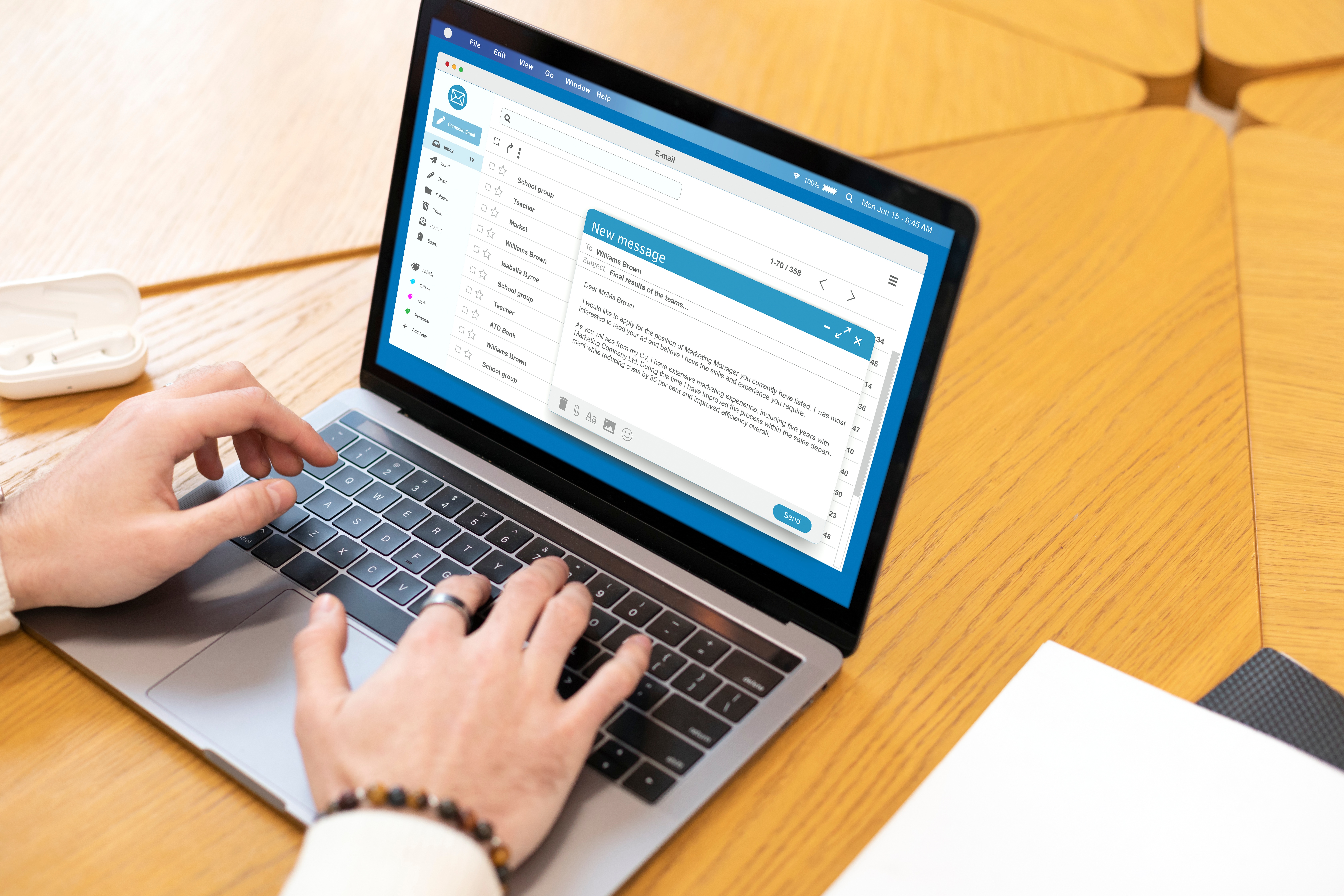 Close-up shot of a professional typing an email on his laptop, sitting at a wooden table