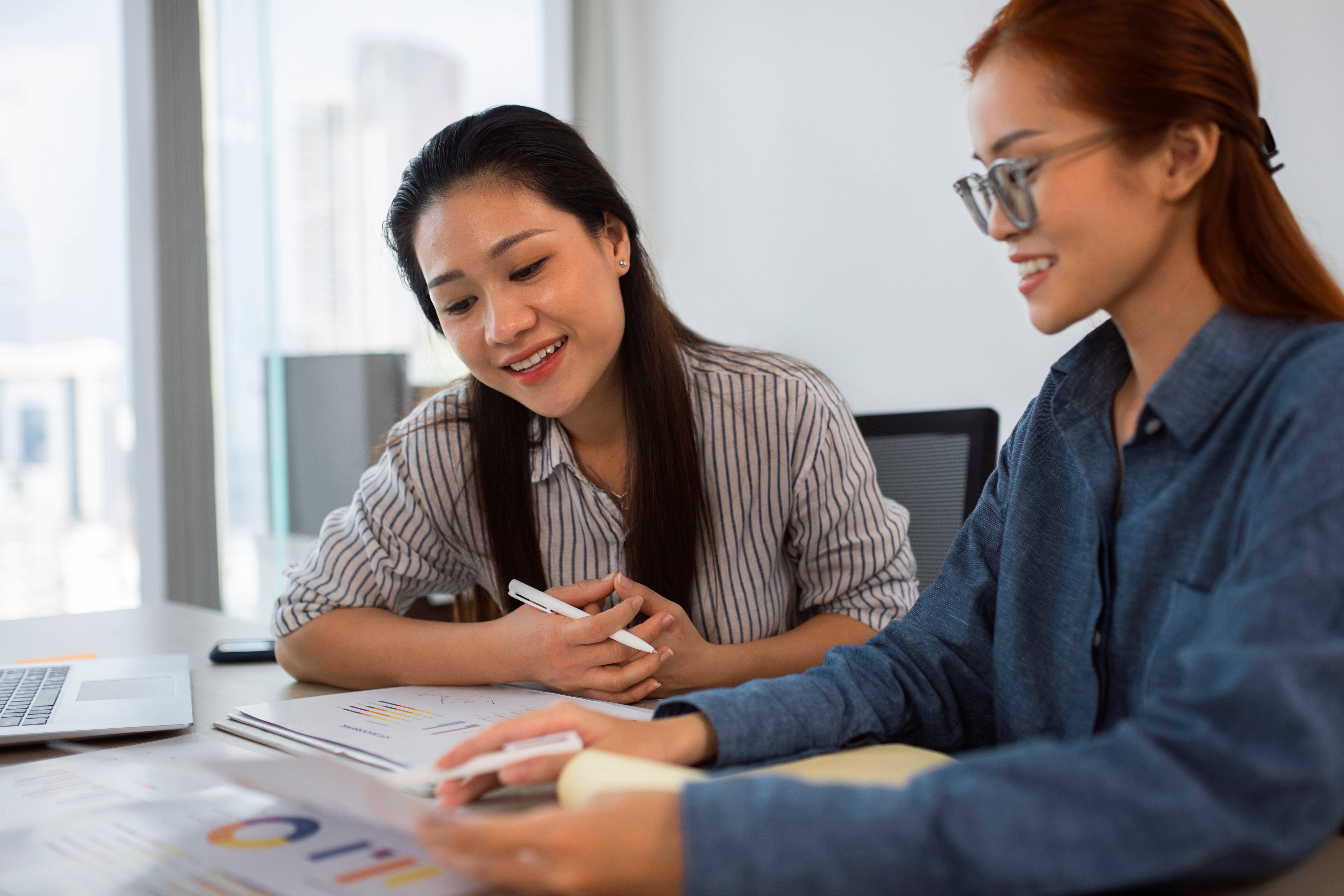 Two female Asian professionals looking at papers covered in graphs and charts