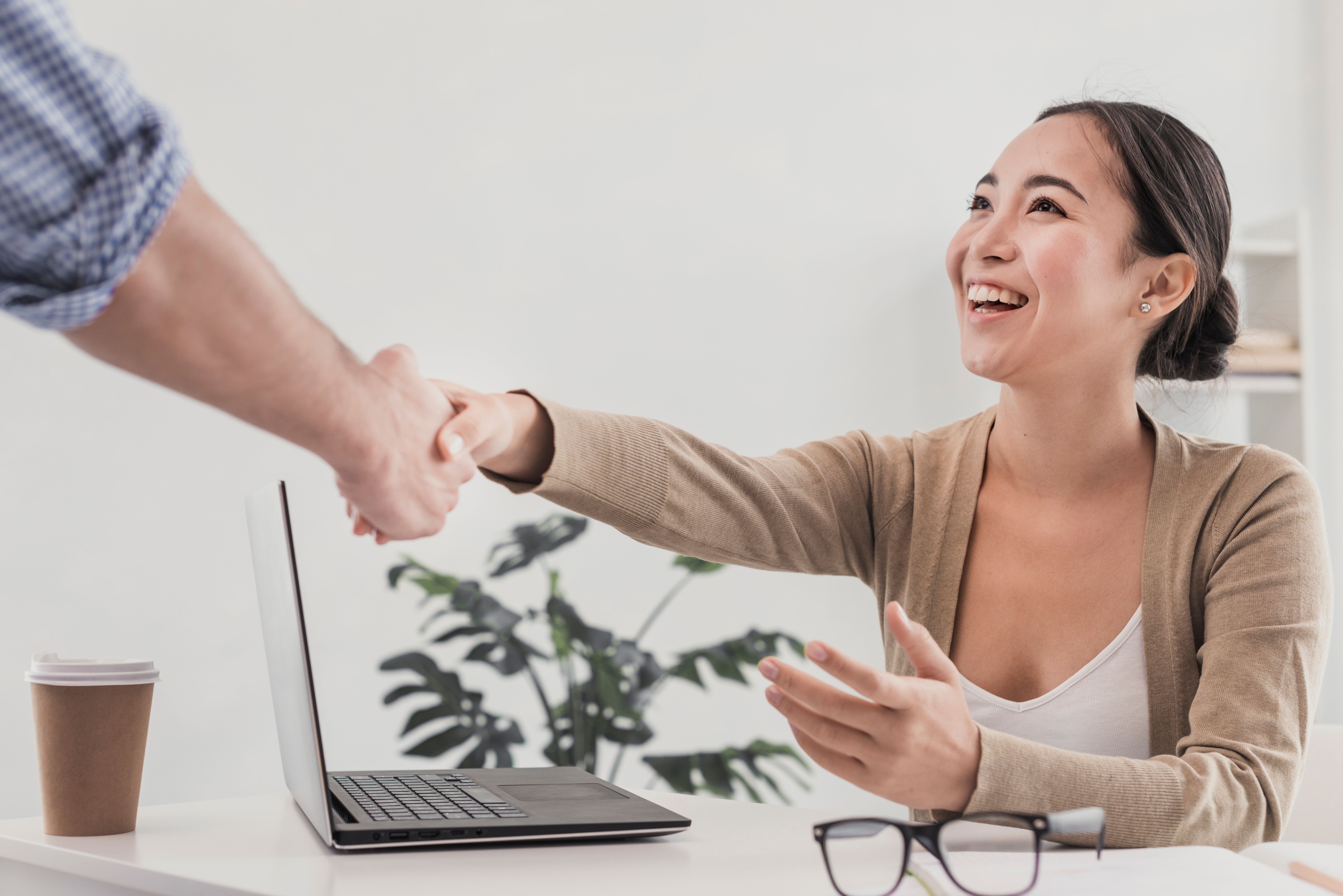 Smiling Asian woman seated at a table shaking hands