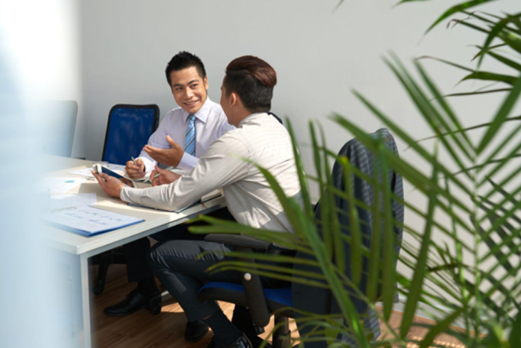 Two cheerful young businessmen are seated at a desk, engaged in a discussion and planning a work meeting.