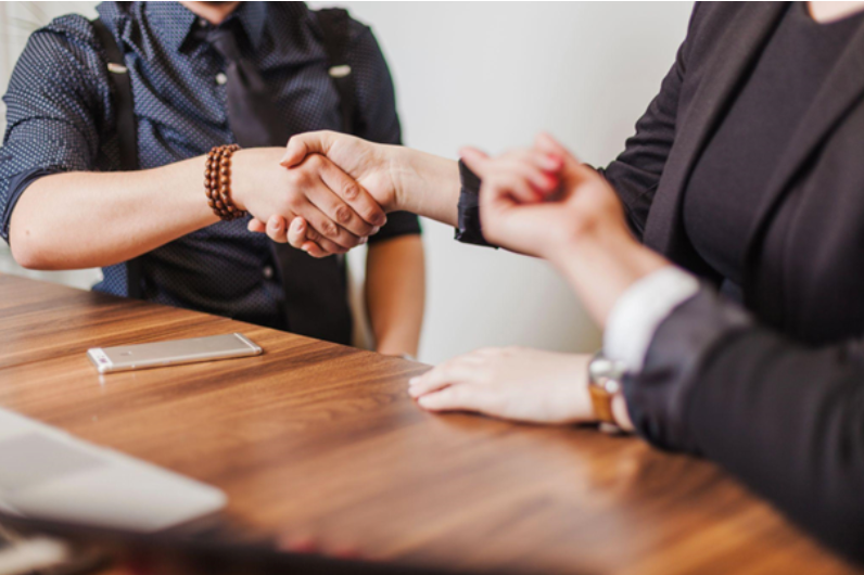 Two people shaking hands over a wooden table, illustrating effective communication and teamwork, key selection criteria examples for building strong professional relationships.