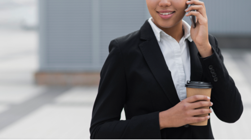 A businesswoman in a suit, holding a coffee cup, smiles while on a phone call, possibly discussing a personal reference for a job opportunity.