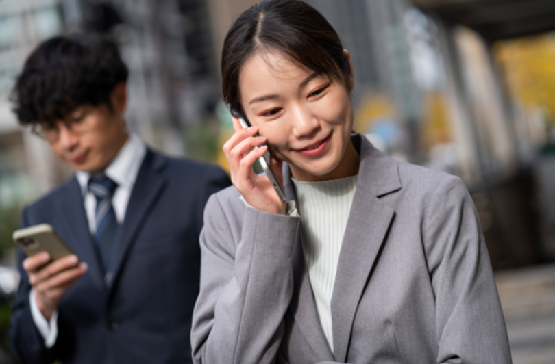 A businesswoman in a suit smiles while on the phone, possibly discussing a personal reference with team colleagues.