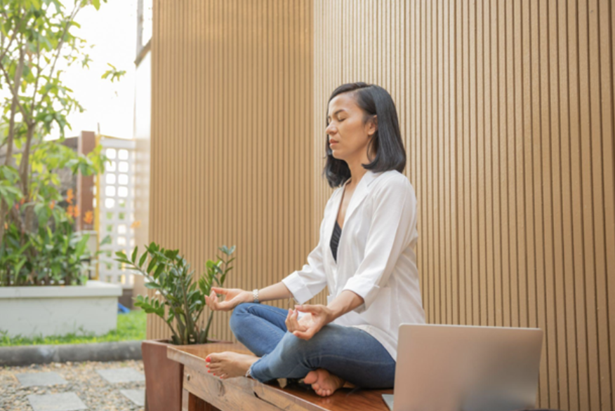 Asian woman sitting cross-legged on bench and meditating