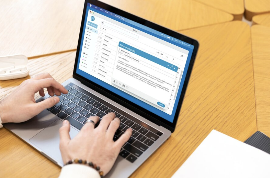 Close-up shot of a professional typing an email on his laptop, sitting at a wooden table