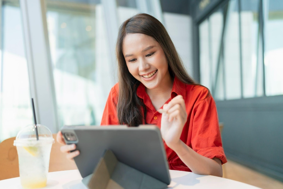 Asian woman smiling at tablet with a drink next to her