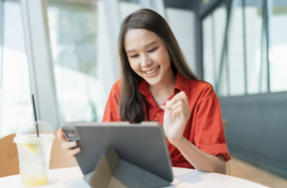 Asian woman smiling at tablet with a drink next to her