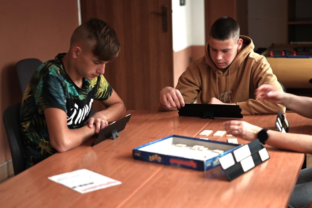 Obóz w Hucie Różanieckiej | Chłopcy siedzą przy stole grając w grę planszową, przed każdym z nich tabliczka z literkami, na środku pudełko z gry..JPG