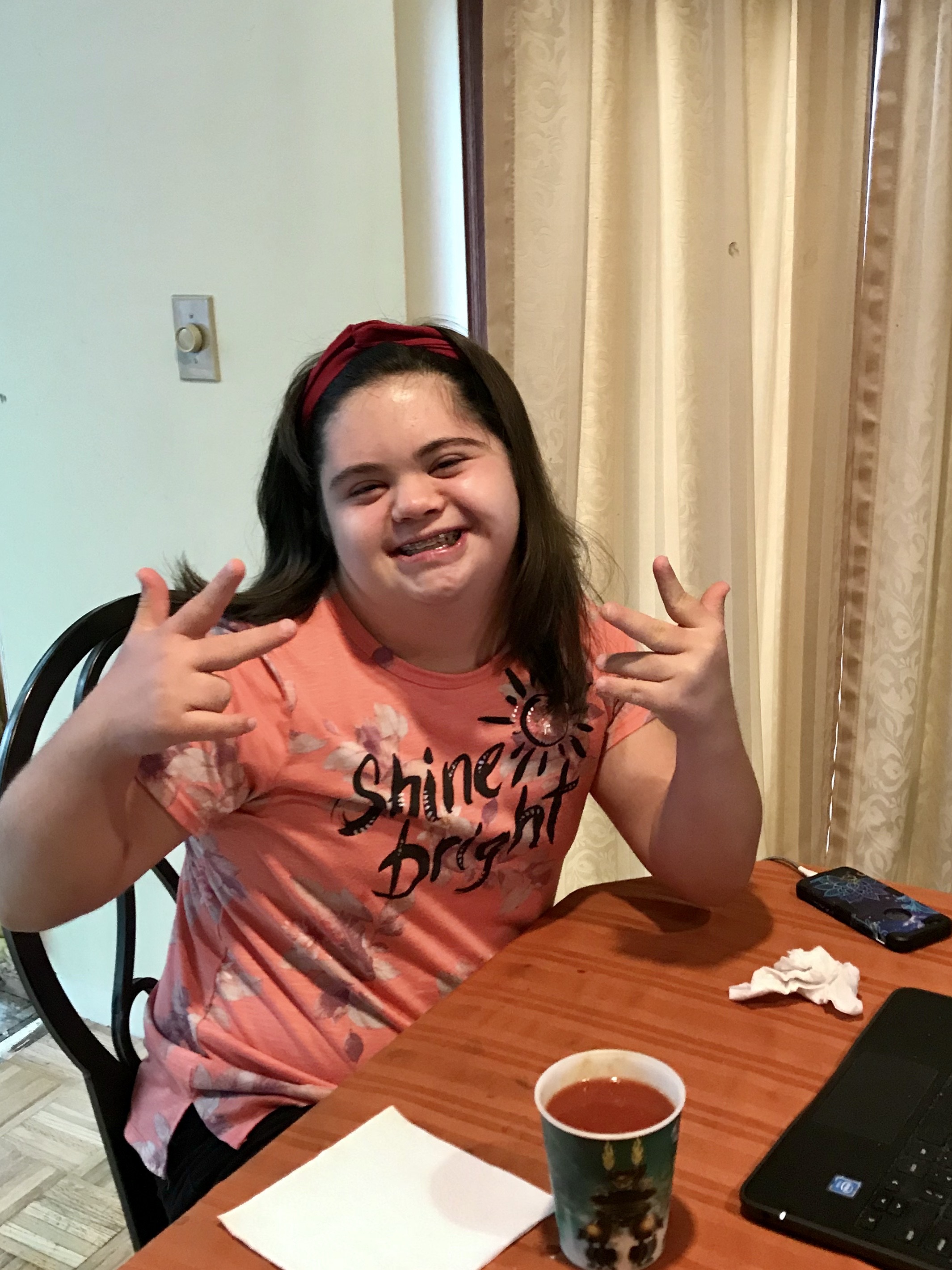 A young lady with down syndrome putting up peace signs with both of her hands and smiling