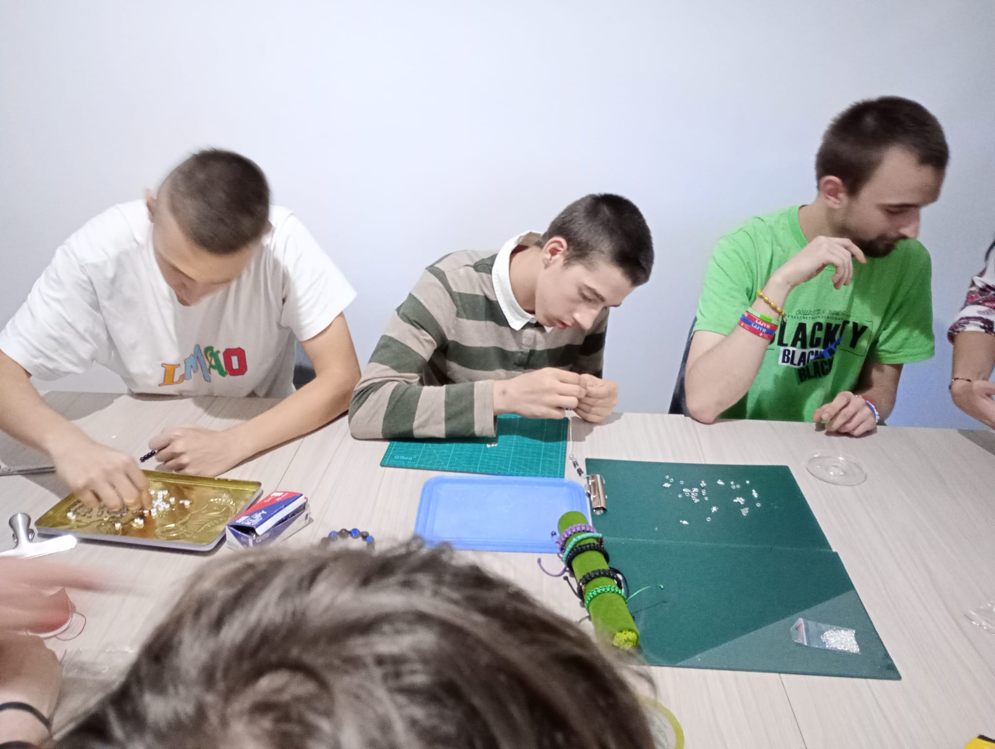 Zajęcia z programu "Fajna ferajna" | Uczestnicy warsztatów siedzą za stołem i nawlekają koraliki rozłożone na podkładkach na blacie..jpg
