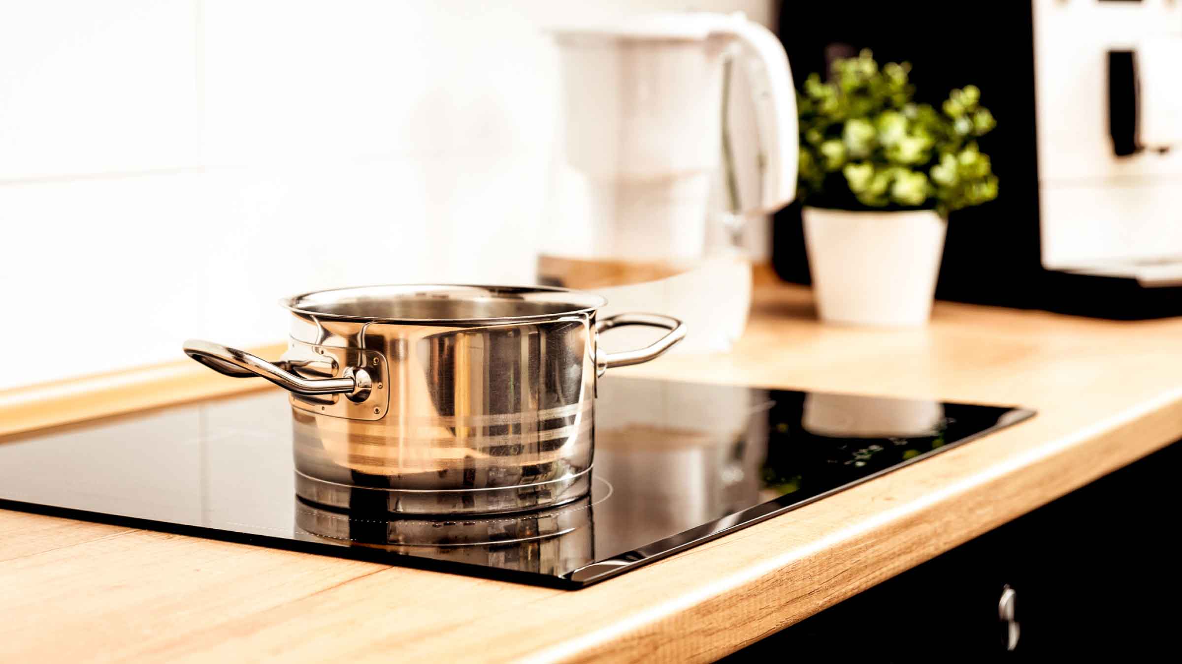 Wooden kitchen counter top, with a black electric stovetop and a silver pot sitting on top.