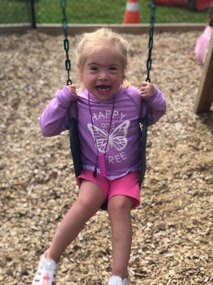 A young girl with down syndrome playing on a swing set