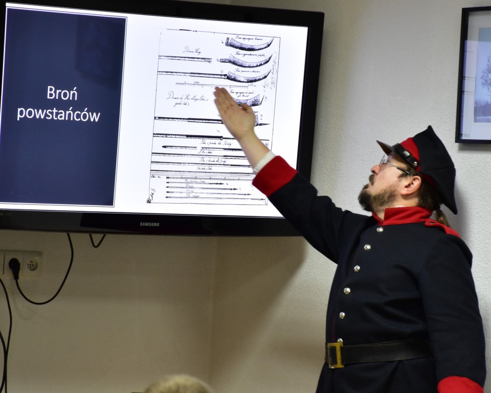 Lekcja historii | Mężczyzna w mundurze Powstańca wskazuje ręką napisy wyświetlane ne ekranie telewizora..JPG