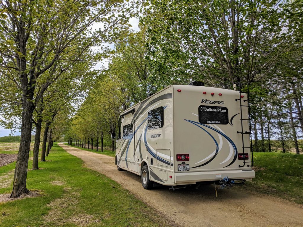 An RV is pictured leaving Green Hill Farm on the dirt path paved in lush trees.