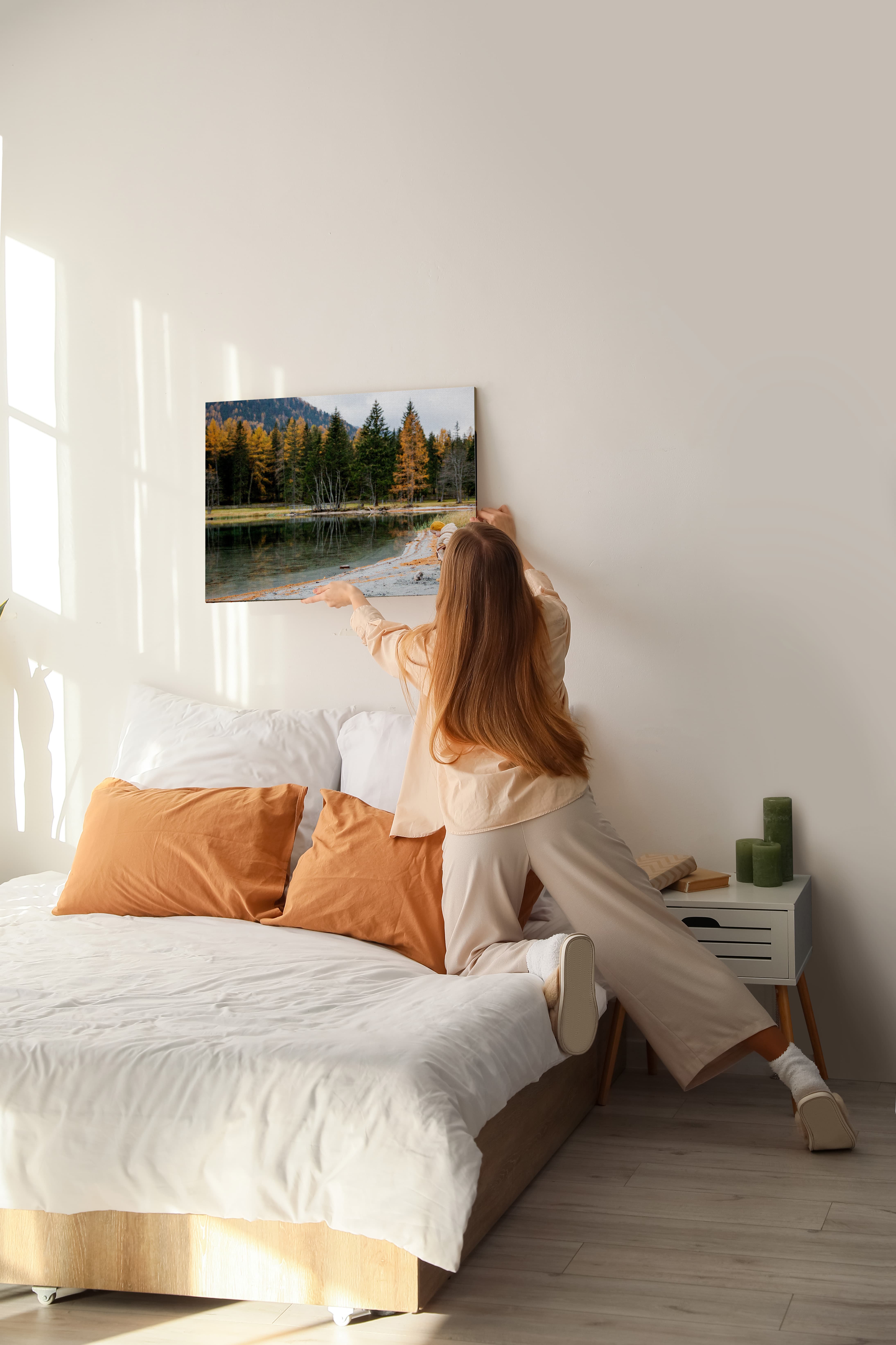 Photo of woman hanging canvas print above bed.