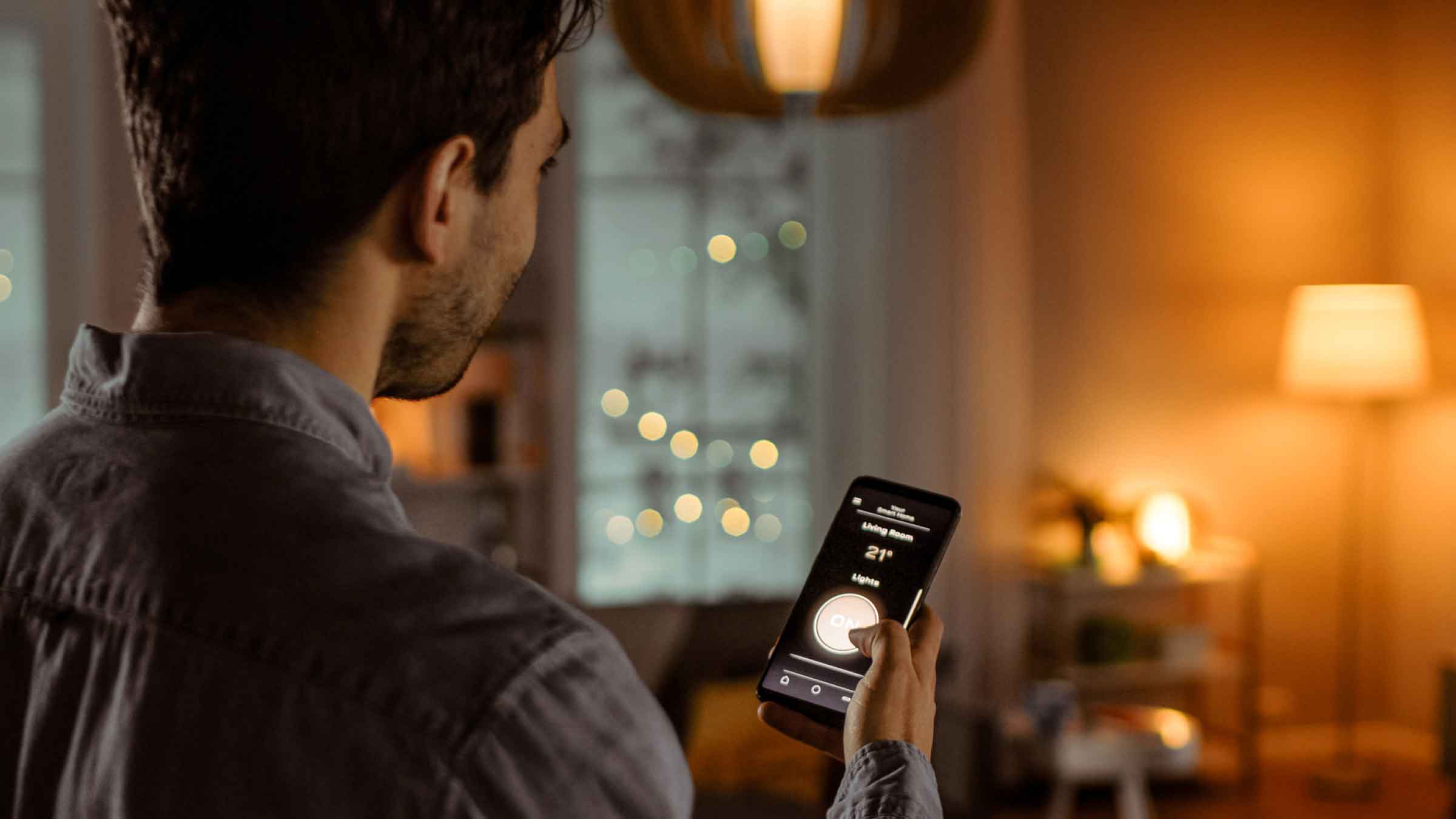 Man holding phone controls the brightness of his living room lights using an app on his phone.